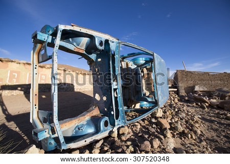 Rusted blue old car frame left in a remote village early in the morning against a blue sky. Bolivia