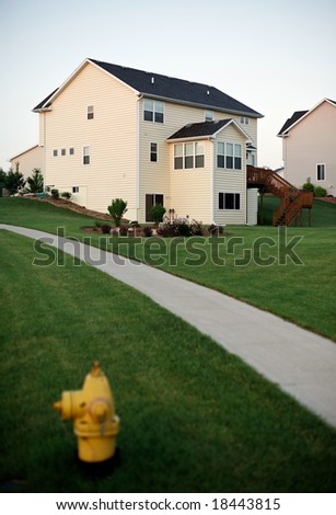 Suburban sidewalk through green lawns with yellow fire hydrant in the foreground and typical suburban house in background - vertical orientation
