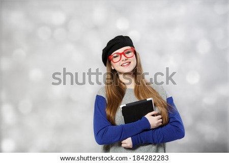 Girl at glasses and beret holds tablet pc at light background