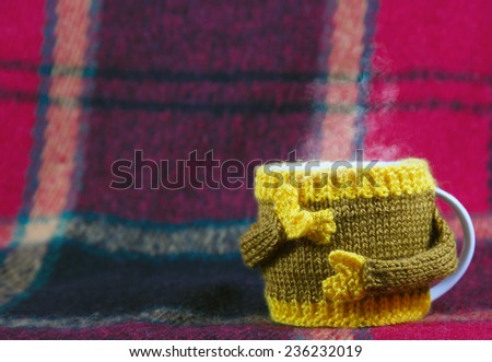 Knitted  yellow cup  at red rug background