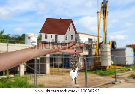 hand with keys and a little house before a construction site / dream of own house