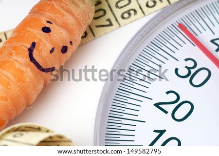 Carrot with a face on a body scale with tape measure / diet