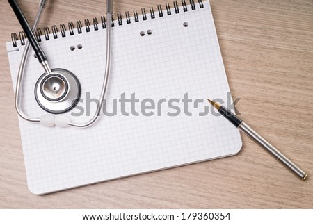 blank writing pad with pen and stethoscope on a table / blank writing pad