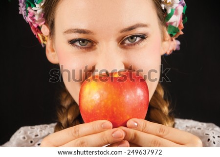 A young beautiful woman with an apple wearing a traditional Polish folk costume on a black background