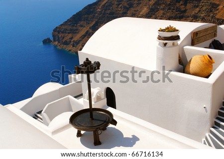 Nice white building with black vintage grape\'s press and amphora on the brink of the rock. Island Santorini, Greece, jule.