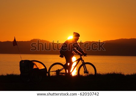 A silhouette of a bicyclist riding his bike along the ocean at sunset