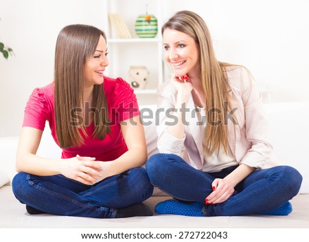 Two girl friends at home talking, having good time, happy and smiling