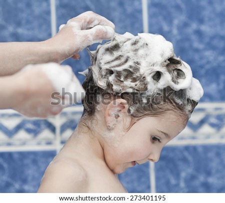 Little cute girl in bath with foam on hair and mother hands washing