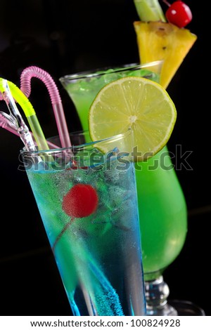 green cocktail with pineapple and blue cocktail with ice and lime on black with reflection