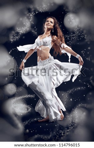 Beautiful active belly dancer woman in white dress over black