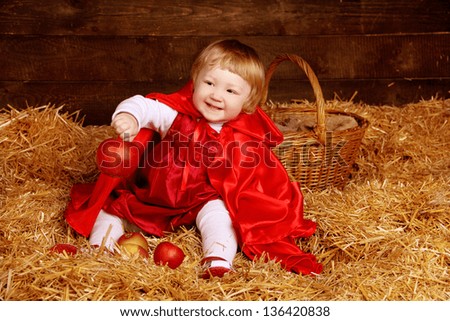 Little girl is sitting on pile of straw with apple. Little Red Riding Hood