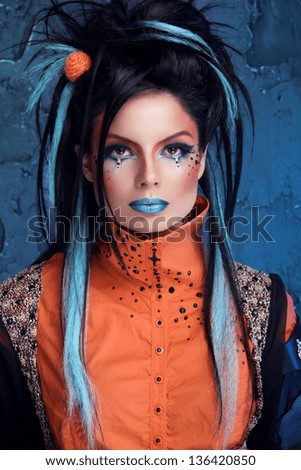 Rock girl with blue lips and punk hairstyle leaning against grunge wall