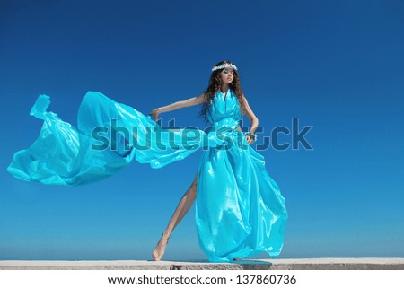 Fashion model woman with blowing dress over blue sky, outdoors