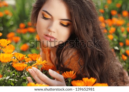 Makeup. Beauty Long Wavy Hair. Beautiful Brunette Woman over marigold flowers. Healthy Hairstyle. Outdoors portrait.