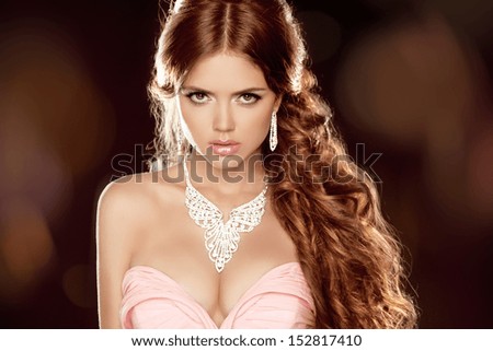 Fashion portrait of beautiful woman with long wavy brown hair style over dark background