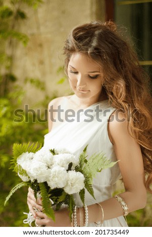 Beautiful young bride holding bouquet of spring flowers with wedding makeup and long wavy hair style, outdoors portrait