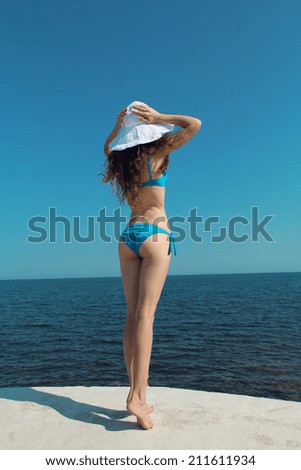 Bikini model woman in white hat over blue sky, outdoors. Brunette girl relax on the beach.