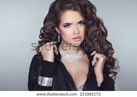 Attractive brunette girl model with long wavy hair styling, makeup and fashion jewelry  isolated on gray background