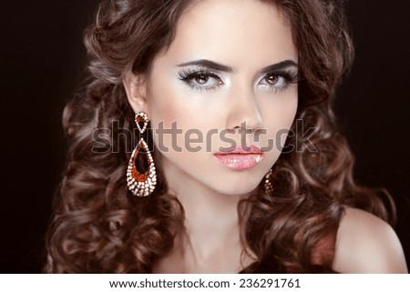 Long hair. Beautiful brunette girl model with fashion earrings. Makeup, luxury jewelry, wavy hairstyle. Woman isolated over dark studio background.