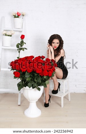 Sexy brunette woman with bouquet of red roses against th wall in modern interior apartment
