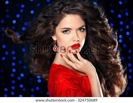 Hair. Beautiful brunette girl model with curly hairstyle, red lips makeup, manicured nails, luxury fashion earring jewelry. Elegant lady over holiday party lights background.