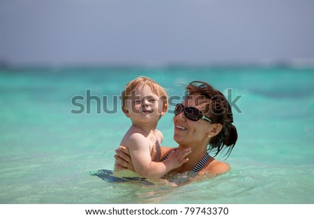 Portrait of a young mother with a cute toddler in her hands in turquoise water