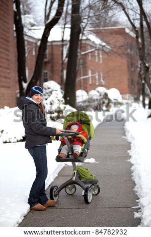 Young mother pushing a stroller with a baby on a warm winter day