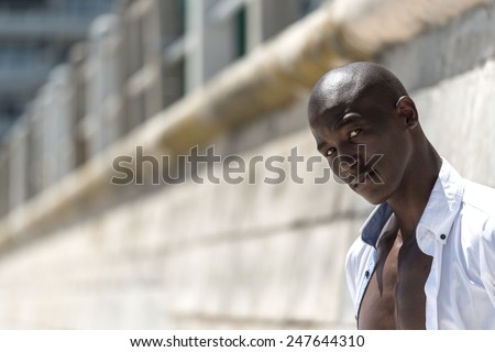 African black man model with six pack in unbuttoned white shirt, isolated against a concrete wall background on the beach