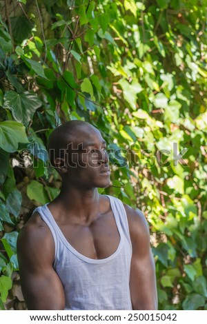Sad black, african american man, thinking against a green plant wall, wearing vest shirt