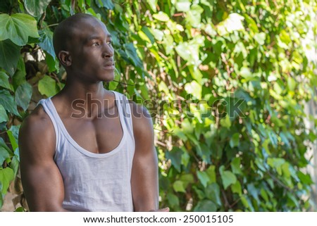 Sad black, african american man, thinking against a green plant wall, wearing vest shirt
