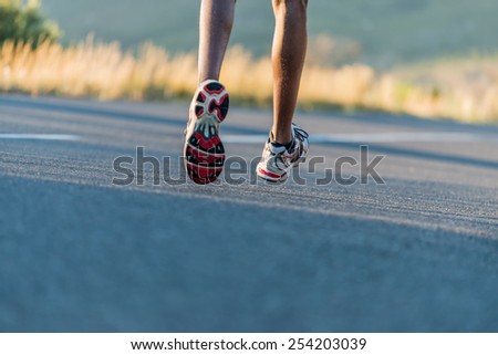 Closeup of an athlete runner\'s feet and shoes running along a road outdoors with a mountain background. Men fitness during sunrise jogging