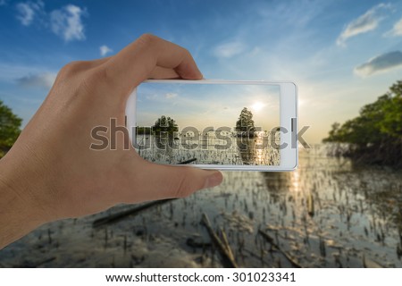 Tourist hand holding smart phone, taking photo of Thailand beach sunset