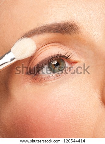 Closeup shot of woman applying eyeshadow on her eyes using makeup brush