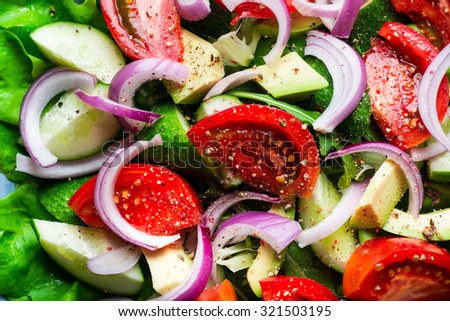 Salad with fresh vegetables on wooden rustic background. Salad with tomato, cucumbers, avocado and onion