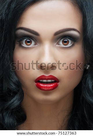 Close-up studio portrait of beautiful young woman with bright makeup and hairstyle looking surprised