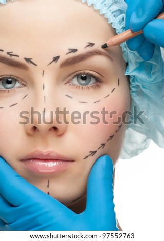 Beautiful young woman with perforation lines on her face before plastic surgery operation. Beautician touching woman face.