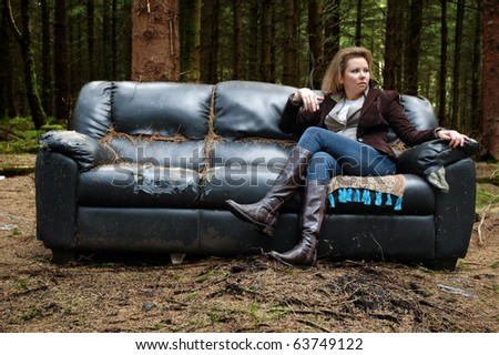 Young smoking woman sitting on the old sofa in the forest