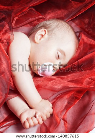 The one-year baby sleeping and wrapped up in red calico material. Close-up.
