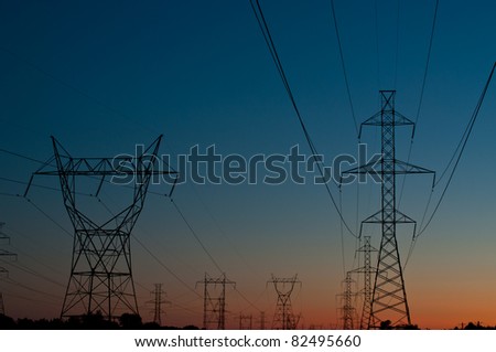 A long line of electrical transmission towers (electricity pylons) carrying high voltage lines in the city at sunset.