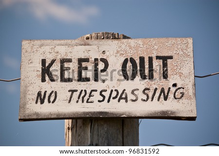 A weathered sign nailed to a fencepost that reads: Keep Out - No Trespassing. Black letters on white sign.
