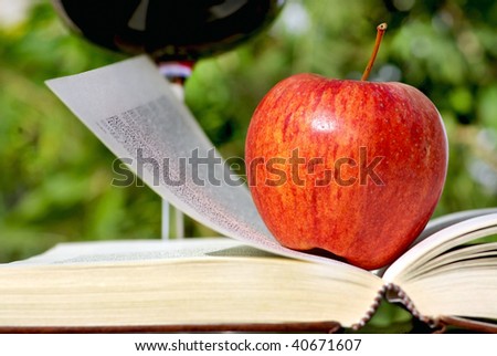 Red apple on book and glass of wine.