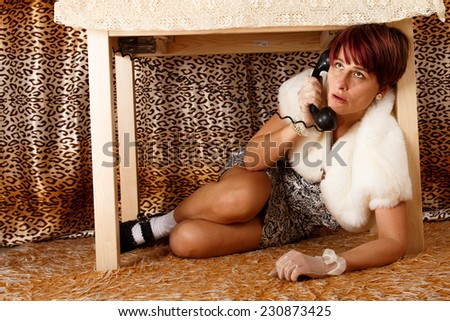 Phoning terrified woman hiding under the table