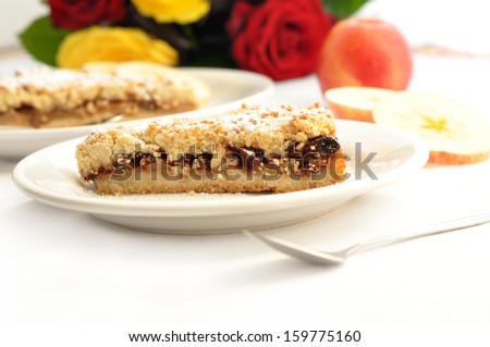 A slice of delicious apple pie with apple slices and roses in the back