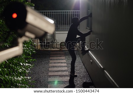 Thief wearing black suit with balaclava and glove being caught by CCTV, surveillance camera during sneak into a house at night Foto stock © 