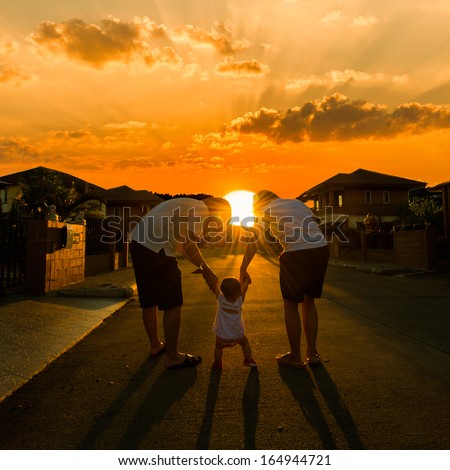 Parents escourting their child to walk together in street at sunset
