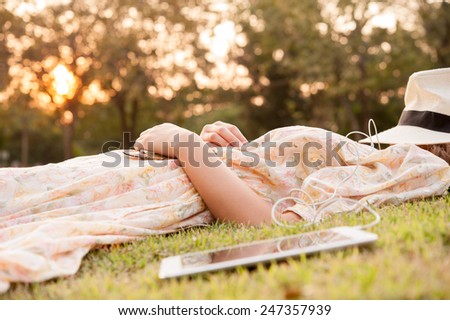 Young woman taking a nap in park with hat over face with tablet
