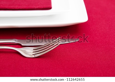 Cutlery and white square plates on red tablecloth