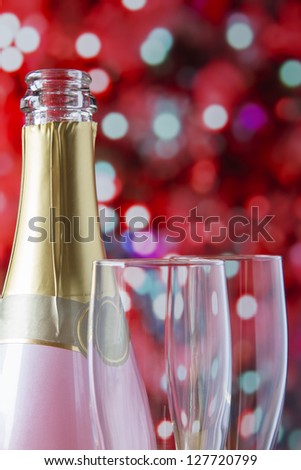 Pink sparkling wine bottle with flutes on red festive light background