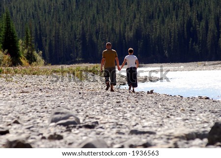 man and woman walking hand in hand near a river in nature park