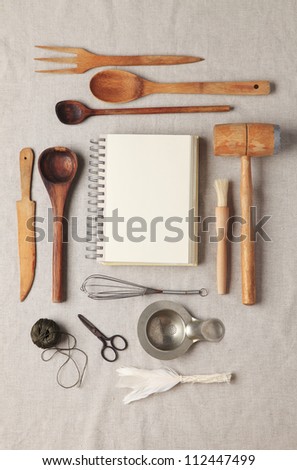 Blank recipe book or shopping list with wooden kitchen utensil on a tablecloth